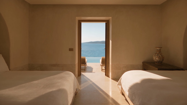 Schlafzimmer in hellem Stein mit Blick durch die offene Tür auf das Meer